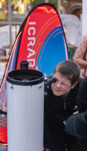 A young boy crouching down, looking through a large telescope pointing at the sky.